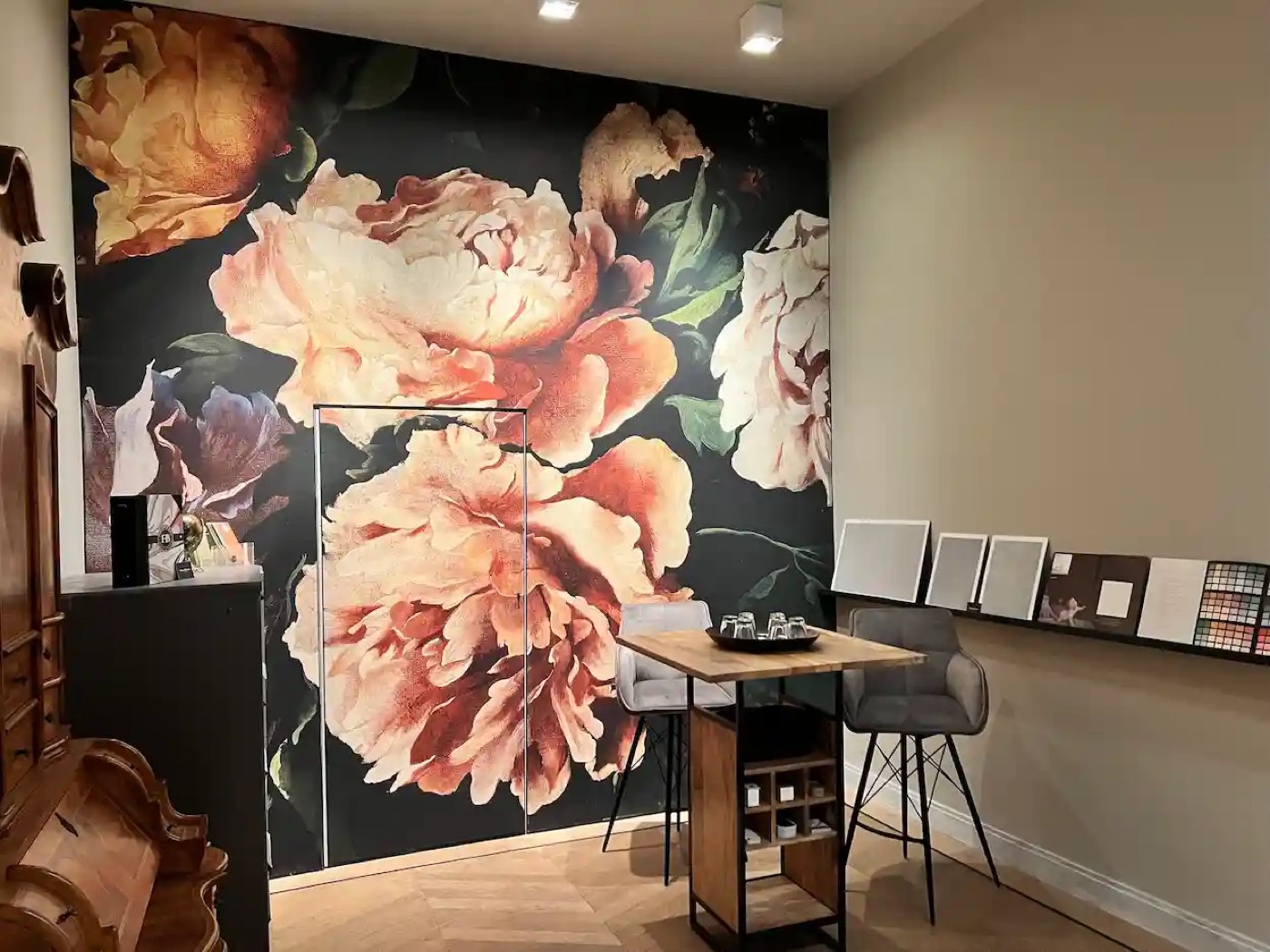 Showroom mit großformatiger Blumentapete, Holztisch und Farbmusterkarten an der Wand